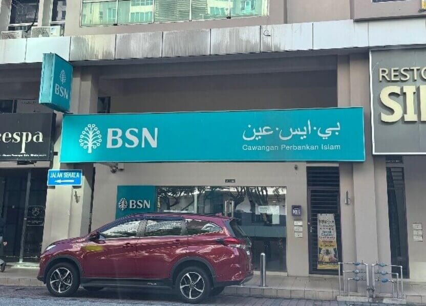 Pandangan hadapan cawangan Bank Simpanan Nasional (BSN) Cawangan Perbankan Islam dengan papan tanda besar berwarna biru muda di tingkat bawah bangunan komersial, serta sebuah kereta SUV berwarna merah gelap diletakkan di bahagian hadapannya