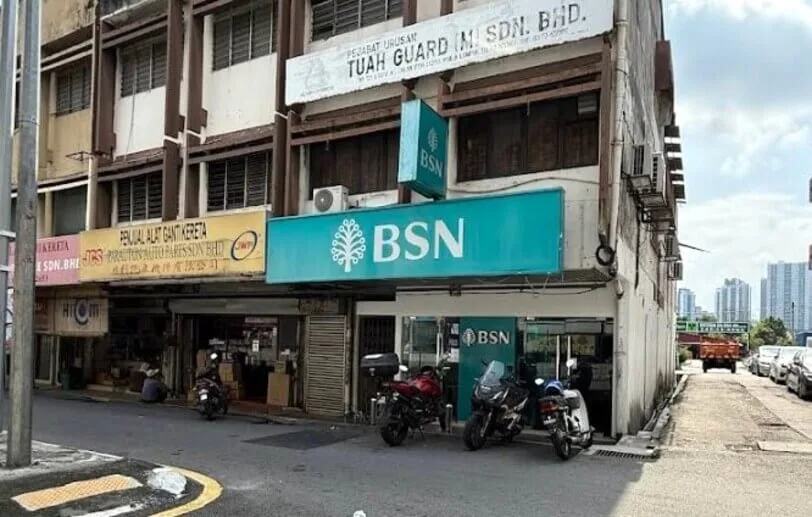 Papan tanda hijau pirus Bank Simpanan Nasional (BSN) di tingkat bawah bangunan kedai lot tepi, bersebelahan kedai alat ganti kereta dan di bawah pejabat Tuah Guard Sdn. Bhd.