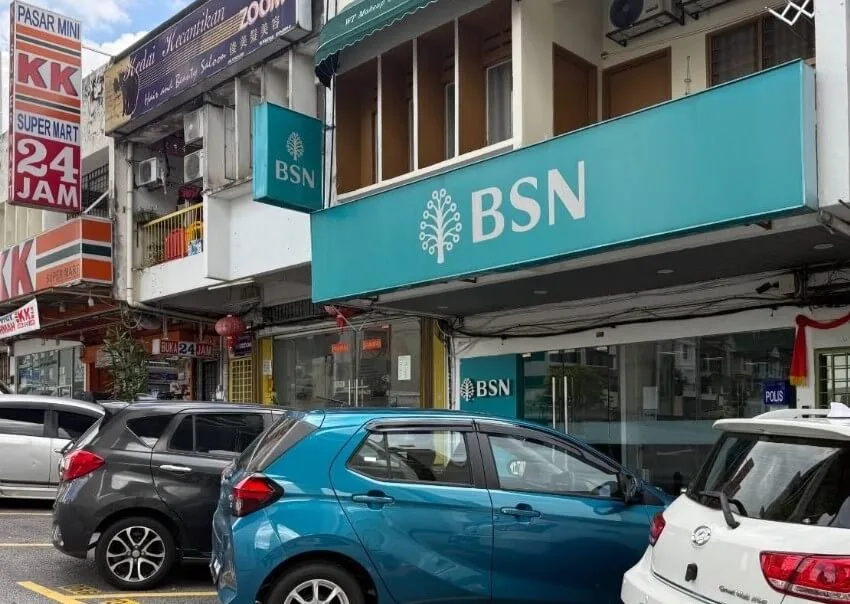 Pandangan hadapan cawangan Bank Simpanan Nasional (BSN) yang memaparkan papan tanda hijau kebiruan (teal) dengan logo BSN. Kelihatan beberapa buah kereta diletakkan di petak meletak kereta di hadapan premis, berhampiran kedai KK Super Mart