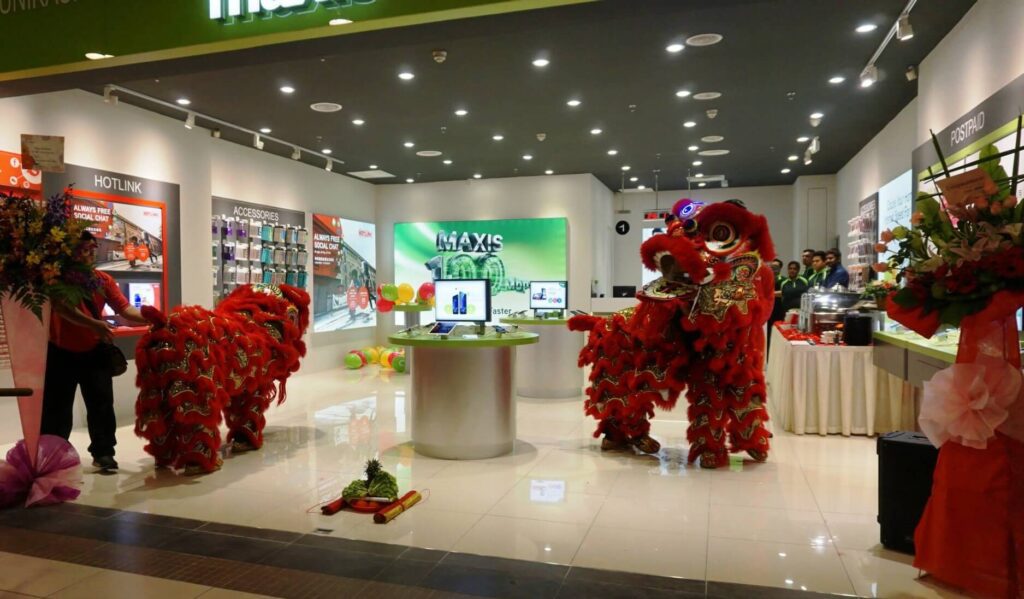 Dua penghibur dalam pakaian Barongsai merah terang dan emas menari di dalam kedai telekomunikasi Maxis moden yang terang benderang