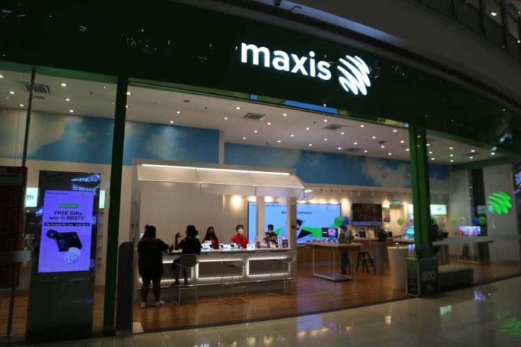 Gambar dalaman Maxis Center NU Sentral yang terletak di pusat membeli-belah. Kedai ini menampilkan reka bentuk moden dengan tingkap kaca besar dan logo "maxis" yang bercahaya di atas pintu masuk. Di dalamnya, terdapat kaunter berbentuk U yang bercahaya terang tempat kakitangan duduk dan berinteraksi dengan pelanggan
