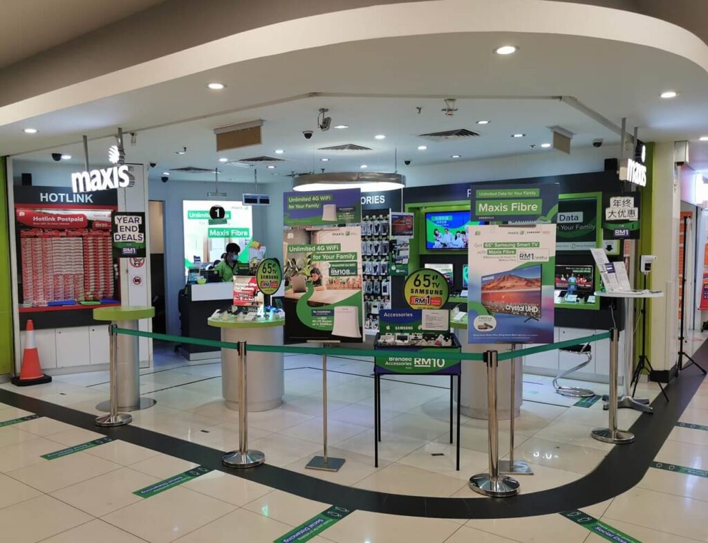 Etalase Maxis di dalam pusat beli-belah. Kedai ini mempunyai skema warna hijau dan putih yang menarik, mengiklankan pelbagai tawaran termasuk 'Maxis Fibre' dan 'Hotlink Postpaid' dengan 'YEAR END DEALS'