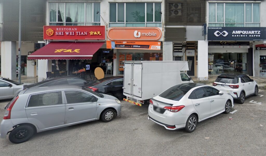 Imej menunjukkan cawangan atau kiosk U Mobile Taman Gaya Ulu Tiram - Tyfong Broadband House Sdn Bhd. Terletak di lokasi yang mempunyai banyak gerai, di sebelah kanan terdapat gerai untuk restoran Shi Wei Tian dan di sebelah kiri untuk kedai Ampquartz