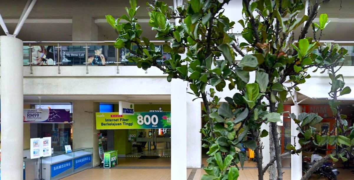 Pemandangan dalaman Maxis Centre di BBT One, Klang, Malaysia. Di latar depan, terdapat pokok pasu dengan daun hijau yang besar. Di latar belakang, sebuah kedai di tingkat bawah memaparkan sepanduk hijau yang besar mengiklankan Maxis Internet Fiber dengan kelajuan 800 Mbps