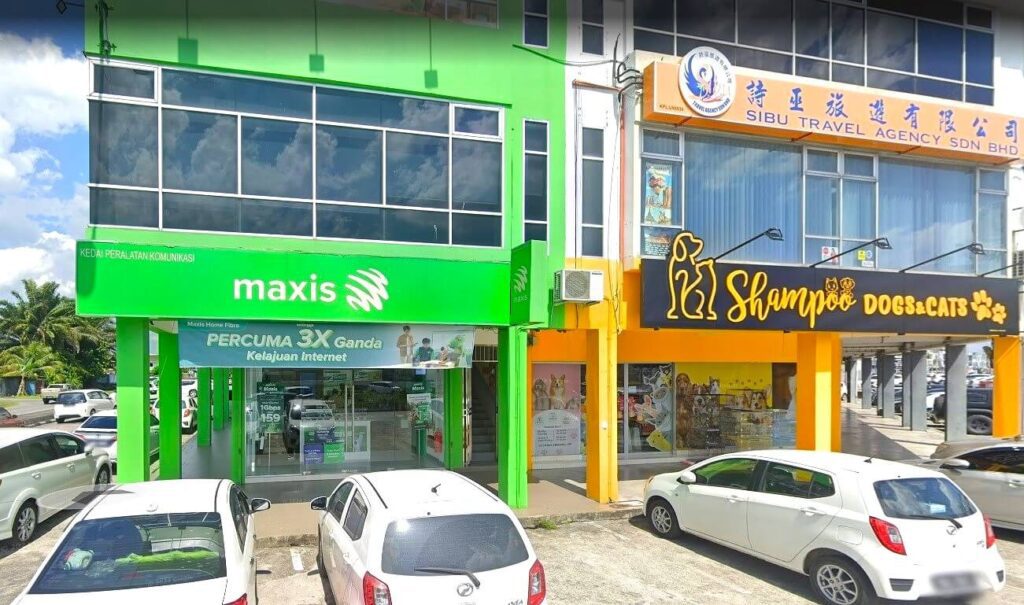 Sebuah bangunan komersial dua tingkat yang meriah di Sibu, Malaysia, adalah rumah kepada beberapa perniagaan. Bangunan di sebelah kiri dicat hijau terang dan mempunyai tanda Maxis Centre yang menarik dalam huruf putih pada latar belakang hijau. Bangunan di sebelah kanan berwarna kuning dan putih dengan papan tanda yang besar