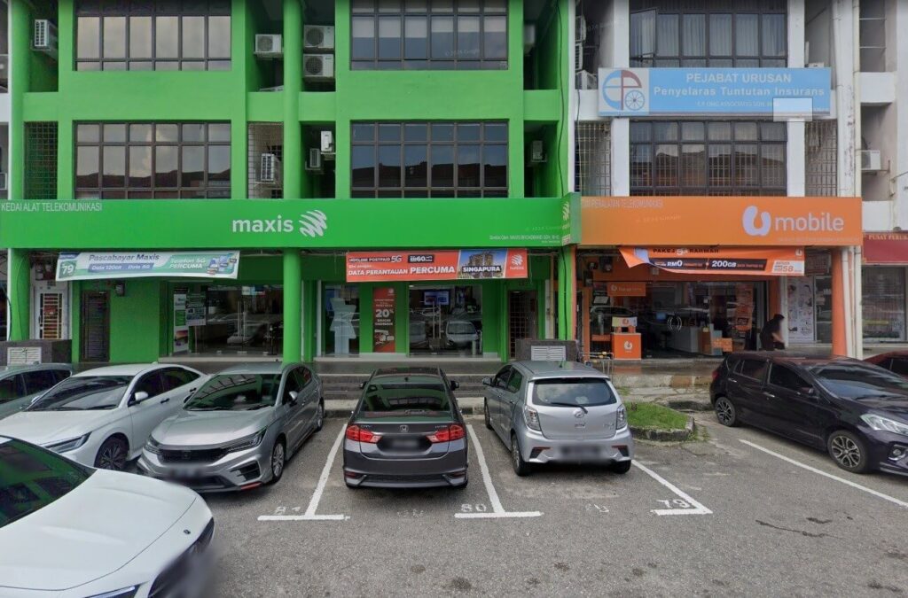 Dua etalase bersebelahan. Di sebelah kiri ialah Maxis Centre Taman Molek dengan fasad hijau terangnya. Tandanya memaparkan perkataan "maxis" dalam huruf putih kecil. Tingkap kaca bangunan di atas memantulkan cahaya sekeliling. Di sebelah kanan ialah kedai U Mobile dengan fasad oren dan logo putihnya