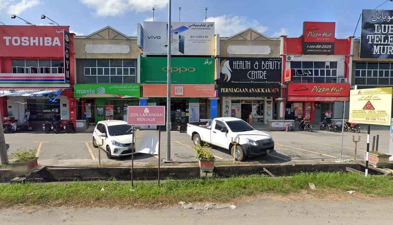 Deretan perniagaan komersial di kawasan pinggir bandar. Dari kiri ke kanan, etalase menampilkan papan tanda Toshiba, etalase Maxis hijau dan bangunan kuning dengan jenama Vivo, Oppo dan Xiaomi. Di sebelahnya terdapat papan tanda merah dan putih untuk Health & Beauty Centre, dan etalase merah dengan dua papan tanda Pizza Hut