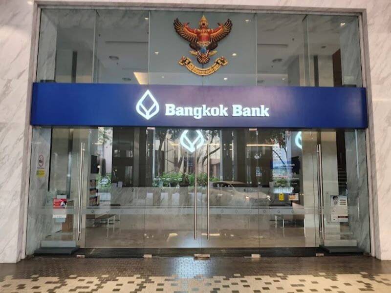 Pintu masuk utama Bangkok Bank Berhad, dengan pintu kaca yang besar. Papan tanda mendatar biru yang mencolok di atas pintu bertulis "Bangkok Bank" berwarna putih, bersebelahan dengan logo berbentuk titisan air mata bank itu. Di atas papan tanda itu terdapat lambang Garuda emas, simbol Kerajaan Thailand, dipasang di dinding