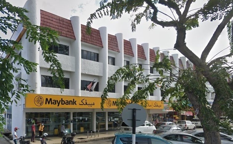 Bangunan cawangan Maybank mempunyai fasad kuning di tingkat bawah dan dinding putih di dua tingkat atas. Bangunan ini mempunyai reka bentuk yang tersendiri, dengan deretan bumbung jubin merah runcing. Beberapa kereta parkir di jalan di hadapan tebing, dan sebatang pokok dengan dahan kosong menutupi bahagian kanan bangunan. Logo dan nama Maybank jelas kelihatan dalam huruf kuning pada fasad, dalam kedua-dua skrip Inggeris dan Arab