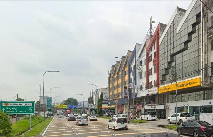 Jalan yang sibuk pada siang hari dengan laluan pejalan kaki yang dicat kuning. Di sebelah kiri, papan tanda jalan hijau menghala ke Kajang dan Kuala Lumpur. Di sebelah kanan jalan, deretan bangunan komersial tiga hingga empat tingkat berdiri bersebelahan. Satu bangunan, dengan tanda Maybank Islamic yang menarik dengan logo kuning, ialah pejabat Maybank Rahang