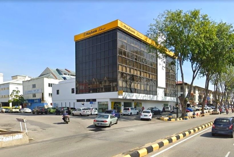 Eksterior Maybank di Temerloh, Malaysia. Bangunan putih, dengan tingkap-tingkap besar berwarna gelap di tingkat dua dan seterusnya, memberikan suasana moden. Tingkat atas ialah blok segi empat tepat dengan bumbung bernada terpampang dengan nama bank, "Maybank," dalam huruf kuning-hitam tebal dan tulisan Arab. Bumbung juga berfungsi sebagai kanopi di atas bahagian trotoar. Beberapa buah kereta diletakkan di sepanjang jalan dan di lot kecil di hadapan bank