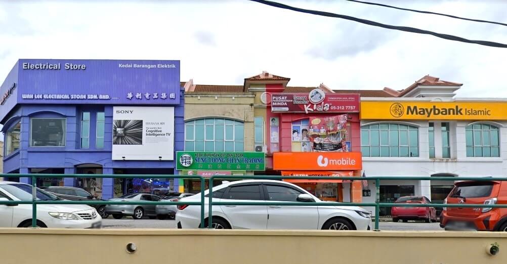 Foto deretan empat bangunan komersial dua tingkat. Dari kiri ke kanan: Bangunan berwarna ungu dengan perkataan "Kedai Barangan Elektrik" di tingkat atas dan papan tanda "Wah Lee Electrical Store Sdn. Bhd." Bangunan berwarna krim dengan fasad berjubin biru dan papan tanda hijau "Seng Loong Lian Trading" di tingkat satu. Bangunan berwarna merah kuning dengan papan tanda "Pusat Tuisyen Minda" dan logo U Mobile di tingkat bawah. Nombor telefon "05-312 7757" kelihatan. Bangunan kuning dengan logo "Maybank Islamic" yang terkenal di tingkat atas dan jam kecil di atas bumbung