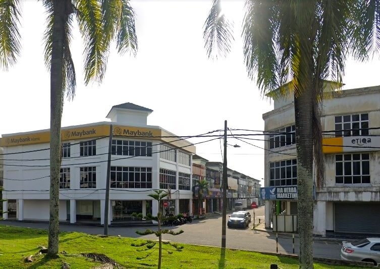 Maybank dua tingkat di Kamunting, Malaysia, dilihat dari seberang jalan. Logo "Maybank" kuning terang dengan simbol harimau kelihatan di bahagian atas dan hadapan bangunan. Bangunan ini mempunyai bumbung rata dan banyak tingkap besar. Terdapat pokok palma di sebelah kiri dan kanan imej, serta di latar depan. Jalan itu dipenuhi dengan bangunan komersial dua tingkat lain, termasuk satu dengan tanda "etiqa" kuning