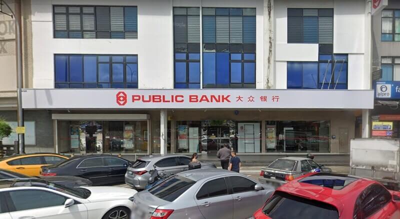 Pandangan hadapan cawangan Public Bank Bukit Indah dengan papan tanda merah dan cina, serta deretan kereta yang diletakkan di hadapan bangunan.