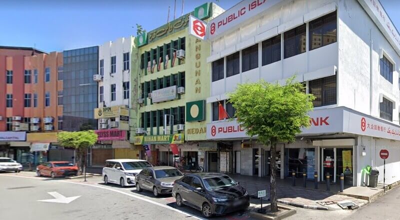 Pemandangan deretan bangunan kedai di tepi jalan, menampilkan cawangan Public Bank Jalan Kota dan beberapa kenderaan yang diletakkan di tempat letak kereta.