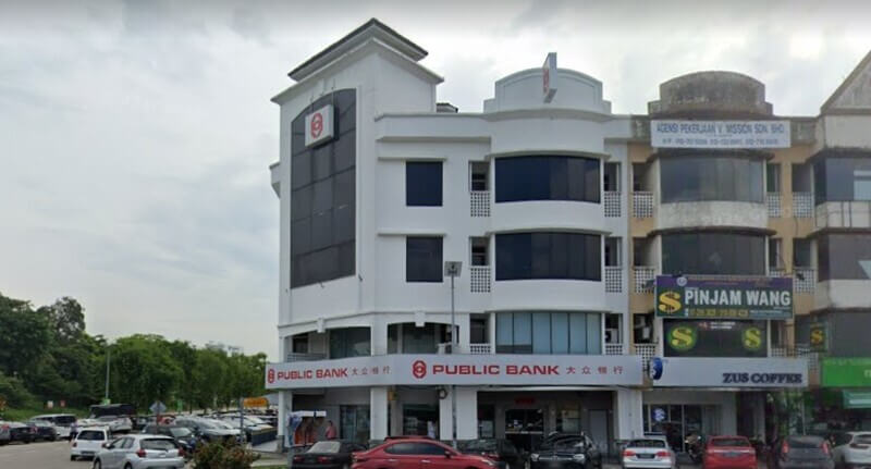 Bangunan cawangan Public Bank Masai putih tiga tingkat di sebelah kedai ZUS Coffee dengan deretan kereta diletakkan di hadapannya.