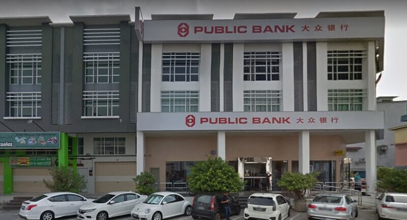 Bangunan cawangan Public Bank di Pekan Nanas dengan papan tanda kedai dalam tulisan Rumi dan Cina, serta kenderaan yang diletakkan di bahagian hadapan.