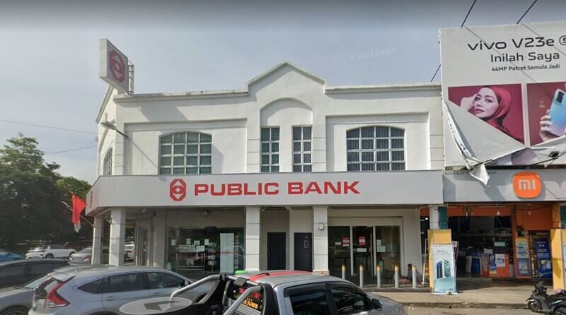 Pandangan hadapan cawangan Public Bank di Pokok Sena dengan papan tanda merah dan kereta diletakkan di hadapannya.