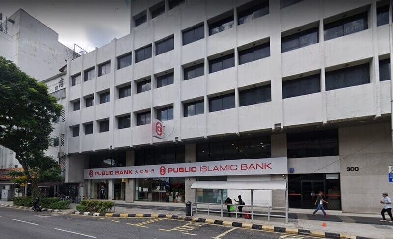 Pemandangan luar bangunan berbilang tingkat berwarna putih yang menempatkan cawangan Public Bank Tiong Nam dan Public Islamic Bank di tingkat bawah. Terdapat papan tanda bank bertulisan merah, perhentian bas di hadapan kaki lima.