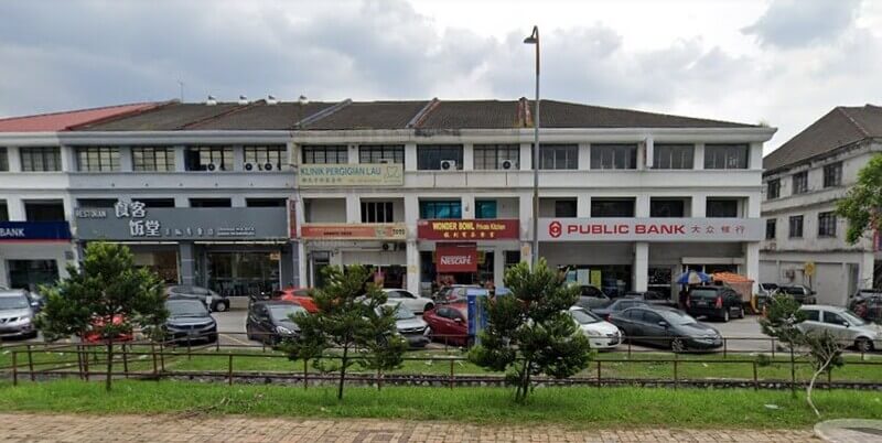 Pemandangan luar bangunan kedai tiga tingkat yang menempatkan cawangan Public Bank di Bandar Sri Damansara. Bangunan ini turut menempatkan kedai-kedai lain seperti restoran dan Klinik Pergigian Lau. Di hadapan bangunan terdapat deretan kereta yang diletakkan di tempat letak kereta serta kawasan rumput hijau di bahagian hadapan.