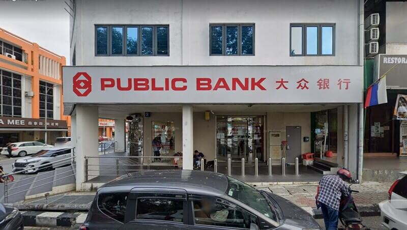 Fasad bangunan cawangan Public Bank Bandar Menjalara bertingkat yang menampilkan papan tanda utama bertulis "PUBLIC BANK 大众银行" dan logo merah. Kelihatan laluan pejalan kaki, pintu masuk kaca, serta beberapa kenderaan.