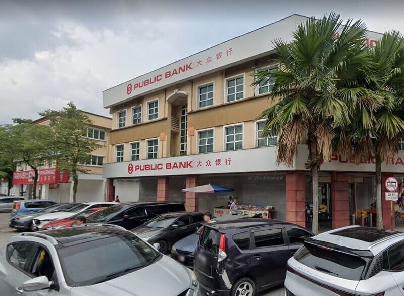 Pemandangan luaran di jalan raya bagi bangunan Public Bank Kepong yang terletak di sudut di Malaysia. Beberapa kenderaan, termasuk kereta dan van, diletakkan di sepanjang jalan.