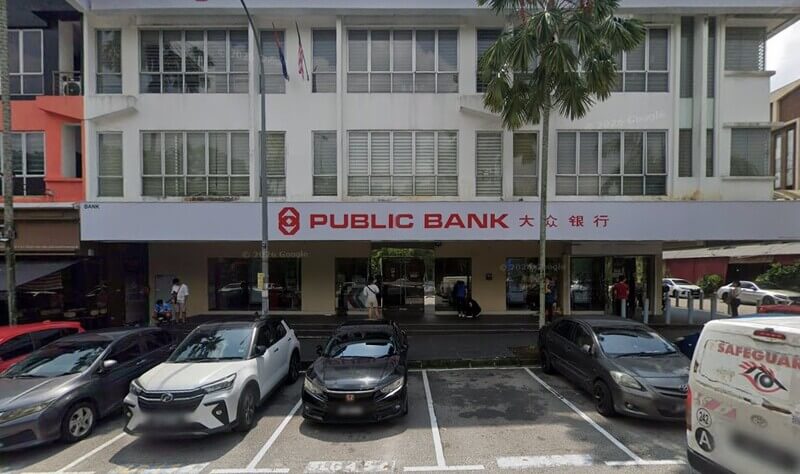 Pandangan hadapan bangunan cawangan Public Bank Sutera Utama dengan papan tanda bercetak nama bank dan beberapa buah kereta diletakkan di petak tempat letak kereta di hadapannya.