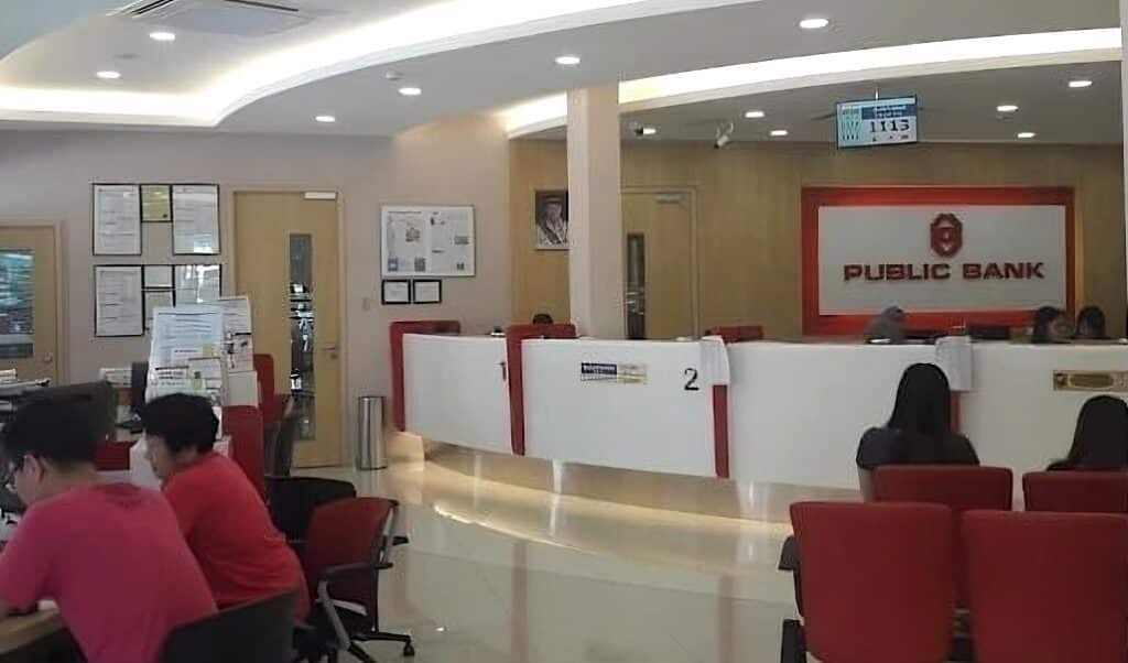 Bahagian dalam cawangan Bank Umum, khususnya kaunter perkhidmatan dan ruang menunggu di Bandar Menjalara. Kawasan perkhidmatan ini menampilkan kaunter putih panjang melengkung dengan aksen merah