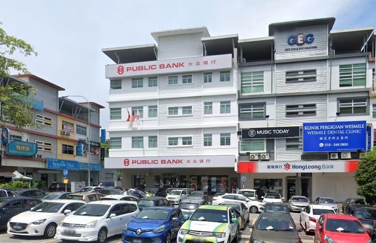 Bangunan komersial bertingkat dengan kawasan parkir yang sibuk di latar depan. Bangunan utama berwarna putih mempunyai tanda Public Bank berwarna merah dan putih di tingkat bawah dan atas, dengan aksara Cina dan Inggeris