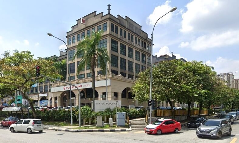 Bangunan berbilang tingkat gaya klasik yang merupakan pejabat cawangan Public Bank di sudut persimpangan yang sibuk. Nama bank itu kelihatan dalam warna merah dan putih di tingkat bawah. Bangunan ini mempunyai fasad coklat muda dengan banyak tingkap dan dikelilingi oleh pokok hijau yang subur dan tumbuhan tropika. Kelihatan papan tanda berwarna putih 'Sentul Boulevard' berhampiran kaki lima