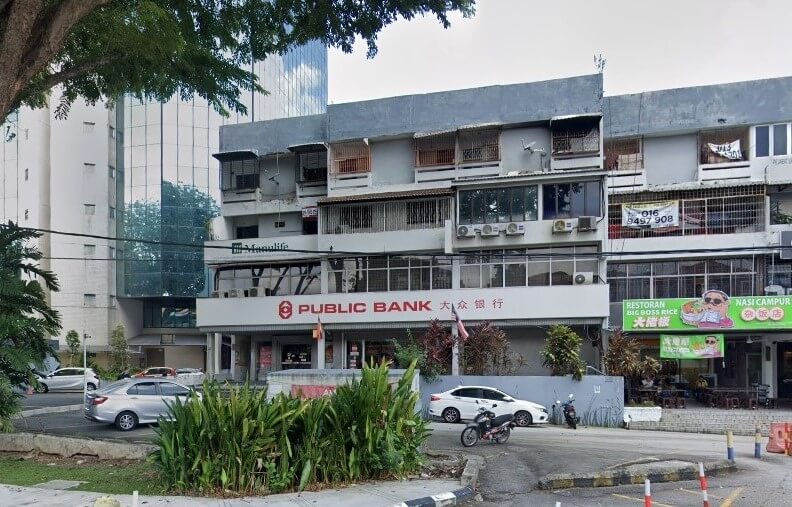 Gambar jalanan cawangan Public Bank Taman Desa di Kuala Lumpur, Malaysia. Bank itu terletak di tingkat bawah bangunan komersial empat tingkat dengan fasad kelabu pudar dan beberapa unit penghawa dingin tingkap. Papan nama bank itu berwarna merah dan putih dengan logo dan nama dalam skrip Inggeris dan Mandarin