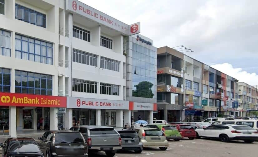 Kompleks bangunan komersial dengan pemandangan aras jalan. Tumpuan utama adalah Public Bank Bandar Baru Permas Jaya, bangunan empat tingkat berwarna putih dengan papan tanda merah-putih. Di sebelah kiri adalah cawangan AmBank, juga dengan papan tanda merah-putih. Bangunan itu adalah sebahagian daripada deretan rumah kedai yang berterusan, dengan beberapa perniagaan lain kelihatan
