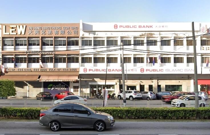 Pemandangan jalan dari bangunan Public Bank and Public Islamic Bank di Batu Pahat, Johor, Malaysia. Bangunan putih tiga tingkat itu menampilkan logo Public Bank merah dan aksara Mandarin, dengan kereta diletakkan di sepanjang jalan di hadapannya