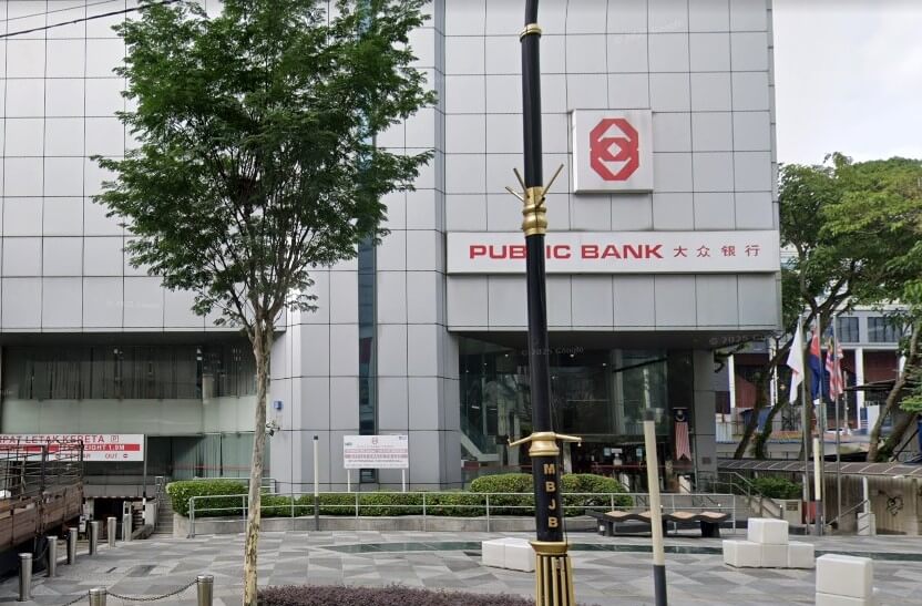 A close-up of the Public Bank Johor Bahru-Bandar Johor Bahru building in Bandar Johor Bahru, Malaysia. Ia adalah sebuah bangunan moden bertingkat dengan fasad berwarna kelabu berkotak-kotak. Nama bank itu ditulis dalam huruf merah besar di bahagian luar, dengan aksara Cina (大众银行) di bawah