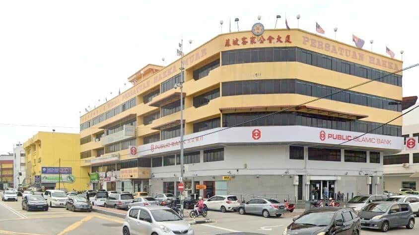 Bangunan kuning besar bertingkat terletak di sudut. Bangunan ini mempunyai bumbung rata dan beberapa tiang bendera. Bahagian atas bangunan dihiasi dengan aksara Cina merah dan papan tanda bertulis "PERSATUAN HAKKA MUAR." Tingkat bawah menempatkan beberapa bahagian hadapan kedai, dengan papan tanda yang menonjol untuk Public Bank dan Public Islamic Bank dari Public Bank Muar