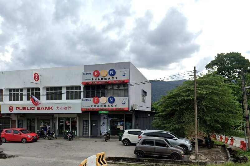 Bahagian hadapan bangunan dua tingkat di Sik, Malaysia, dengan latar belakang langit mendung dan bukit-bukit hijau. Papan tanda Public Bank boleh dilihat di sebelah kiri bangunan, dalam bahasa Inggeris dan Mandarin. Di sebelah kanan, sebuah farmasi terletak di tingkat bawah dan atas, dengan namanya ditulis dalam bahasa Inggeris dan Arab