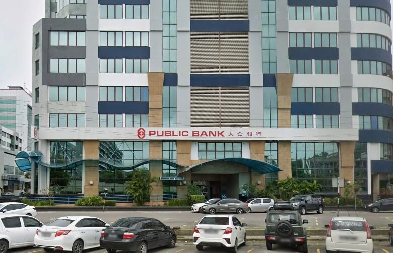 Bangunan Public Bank bertingkat di Kota Kinabalu, Malaysia, dengan pintu masuk aras jalan dan tempat letak kereta berturap yang sibuk penuh dengan kereta di latar depan