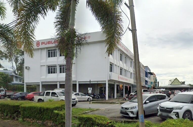 Bangunan tiga tingkat berwarna putih dengan tulisan "PUBLIC BANK" di luar, dikelilingi kawasan parkir dengan beberapa kereta dan pokok palma. Imej tersebut adalah paparan jalan bagi cawangan Public Bank Sri Aman