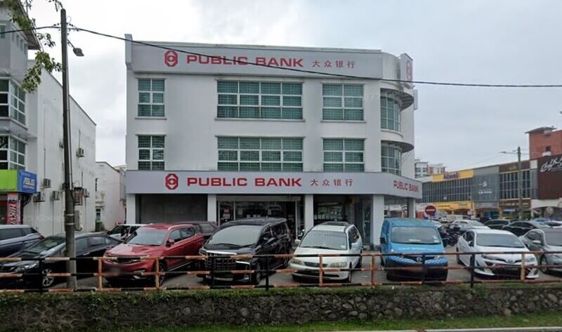 Pandangan hadapan bangunan cawangan Public Bank Air Keroh tiga tingkat dengan kenderaan diletakkan di petak letak kereta di hadapannya.