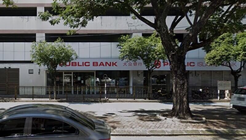 Bangunan Public Bank City Parade dan Public Islamic Bank di tepi jalan, dengan beberapa pokok besar di hadapan serta sebuah kereta melintas di jalan raya.
