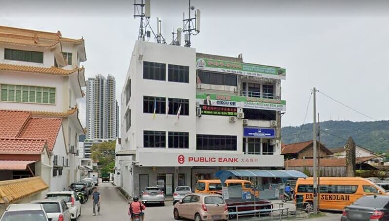 Cawangan Public Bank Jalan Air Itam dengan deretan perniagaan dan kenderaan di hadapan bangunan.