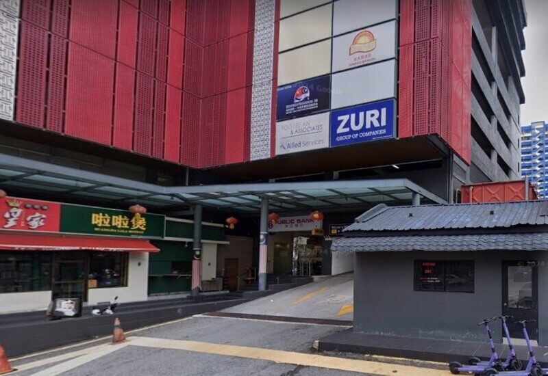 Pemandangan paras jalan bagi bangunan Public Bank di Jalan Bukit Bintang dengan fasad merah, kedai makan di bahagian bawah, dan lorong masuk tempat letak kereta.