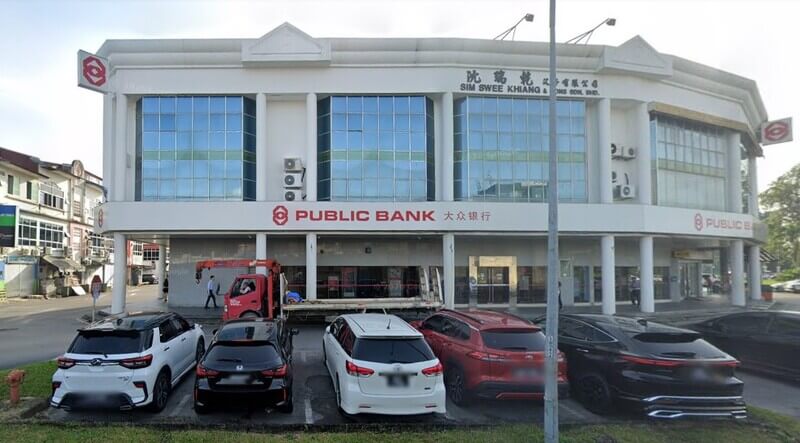 Bangunan Public Bank Jalan Tun Zaidi dua tingkat dengan fasad putih dan tingkap kaca besar, menampilkan papan tanda “Public Bank” dan “Sim Swee Khiang & Sons Sdn. Bhd.”. Beberapa kereta diletakkan di tempat letak kereta di hadapan bangunan.