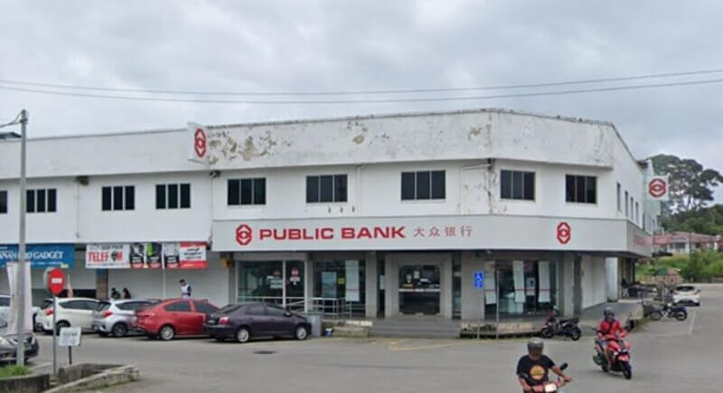 Pemandangan hadapan cawangan Public Bank Masjid Tanah di sebuah bangunan kedai dua tingkat berwarna putih. Papan tanda bank memaparkan tulisan "PUBLIC BANK" bersama tulisan Cina dan logo bank berwarna merah