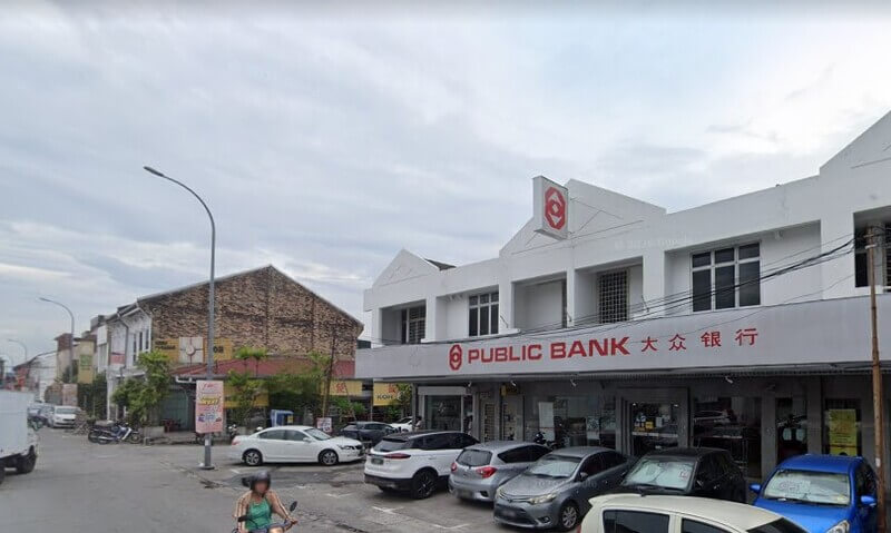 Pemandangan hadapan cawangan Public Bank Menglembu dua tingkat berwarna putih dengan papan tanda merah dan beberapa kenderaan diletakkan di hadapannya.