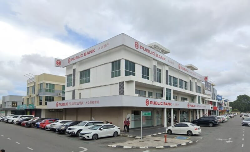 Bangunan tiga tingkat Public Bank di Prima Square dengan fasad berwarna putih, papan tanda Public Bank dalam bahasa Melayu dan Cina, serta deretan kereta yang diletakkan di hadapan bangunan