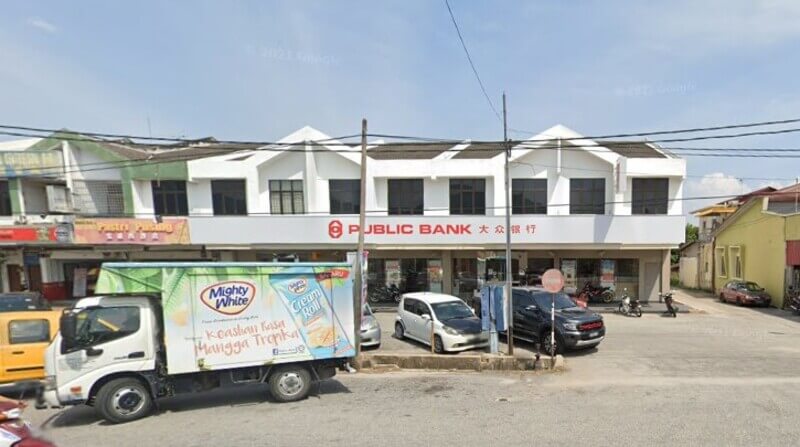 Pandangan hadapan cawangan Public Bank Pusing di kawasan kedai dua tingkat dengan lori penghantaran Mighty White dan beberapa buah kereta diletakkan di bahagian hadapan.