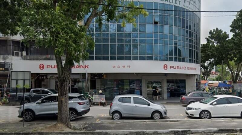 Pandangan hadapan cawangan Public Bank Relau di sebuah bangunan komersial dengan beberapa buah kereta diletakkan di tepi jalan.