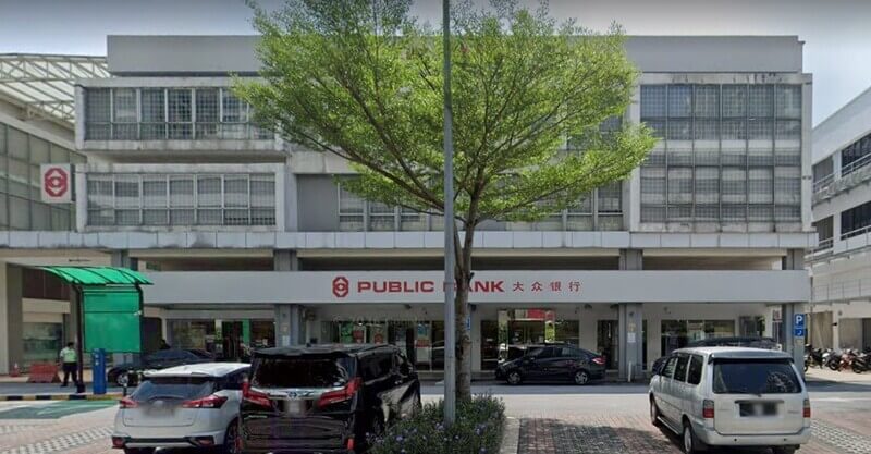 Pandangan hadapan bangunan cawangan Public Bank di Starparc Point dengan papan tanda bank, sebuah pokok di bahagian tengah, dan beberapa kenderaan diparkir di hadapannya.