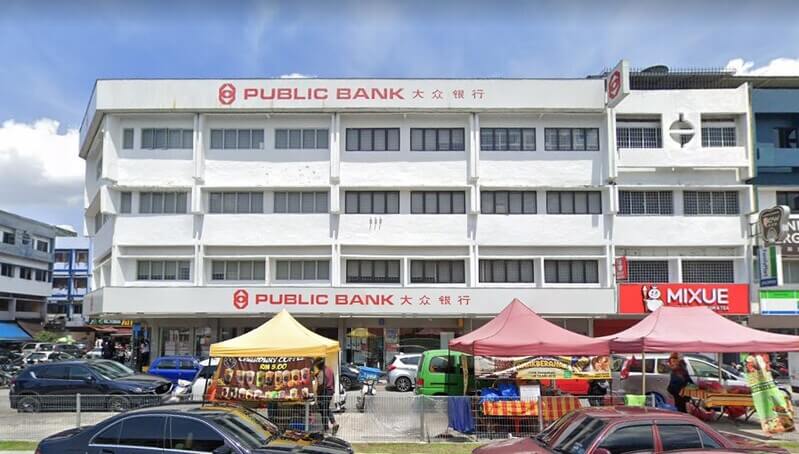 Pandangan hadapan cawangan Public Bank Taman Maluri di bangunan kedai empat tingkat dengan papan tanda merah dan beberapa khemah penjaja di bahagian bawah
